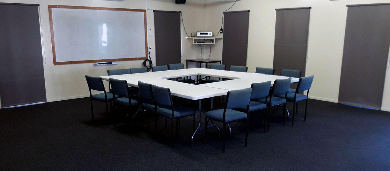 Meeting room with U-shaped table layout, whiteboard, and roller blinds