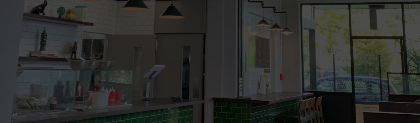 Cafe counter area with green tiled front, shelving, pendant lights, and large windows