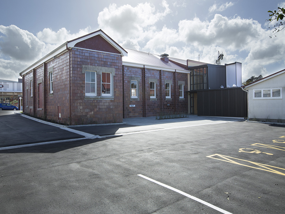 Red-brick hall with white trim and metal extension, viewed from car park