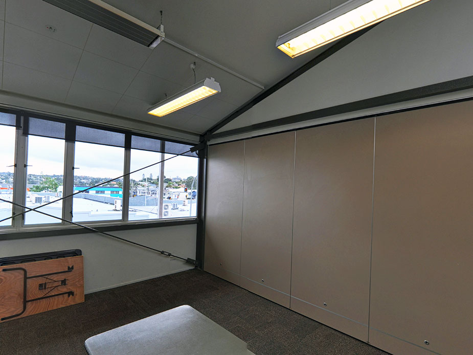 Small plain room with movable partition wall, carpeted floor and fluorescent lighting