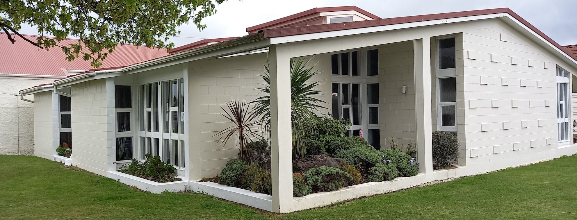 White rendered hall wing with textured block facade, red-tiled roof, and garden border