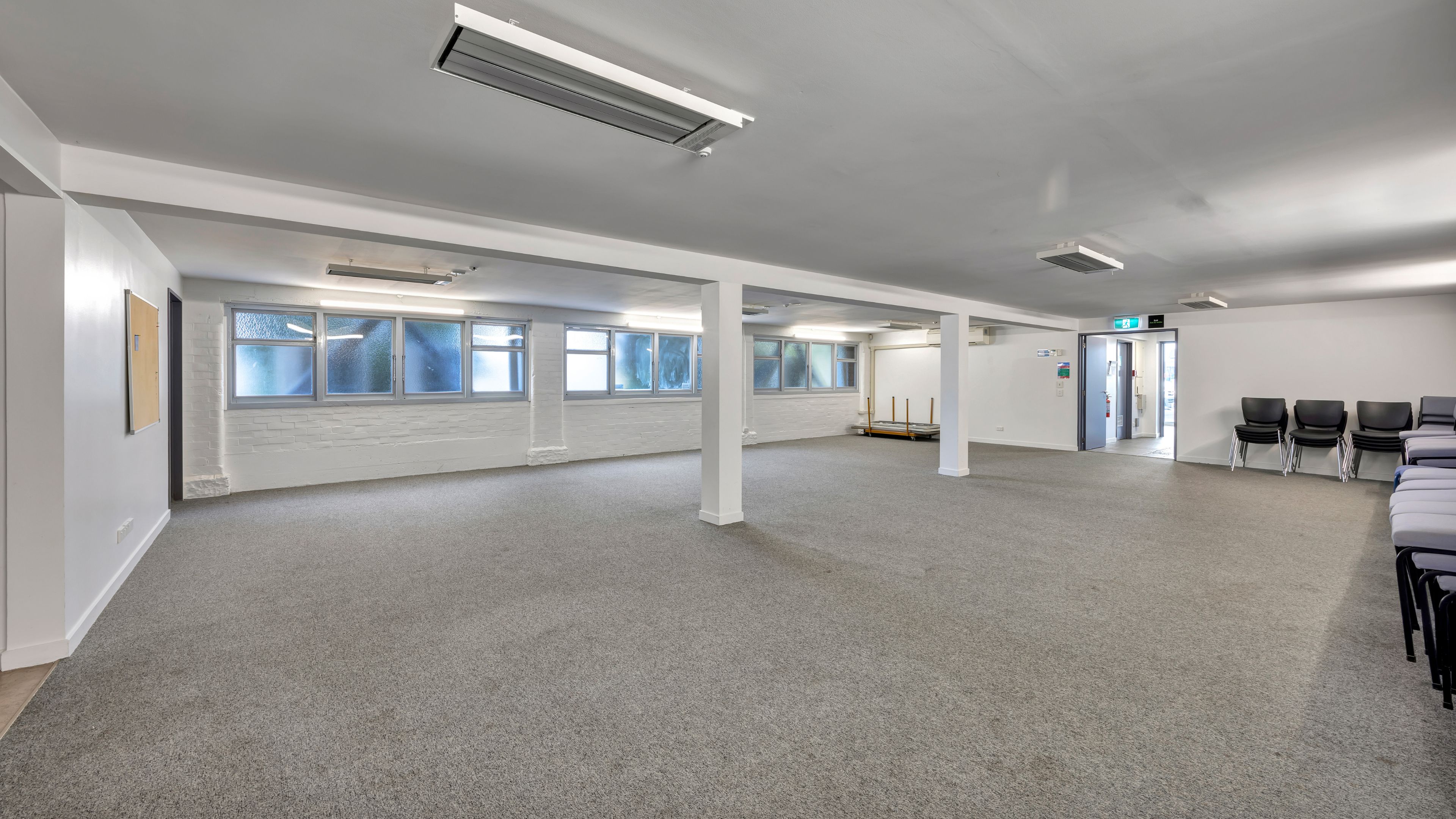 Plain carpeted room with columns and stacked chairs along the wall