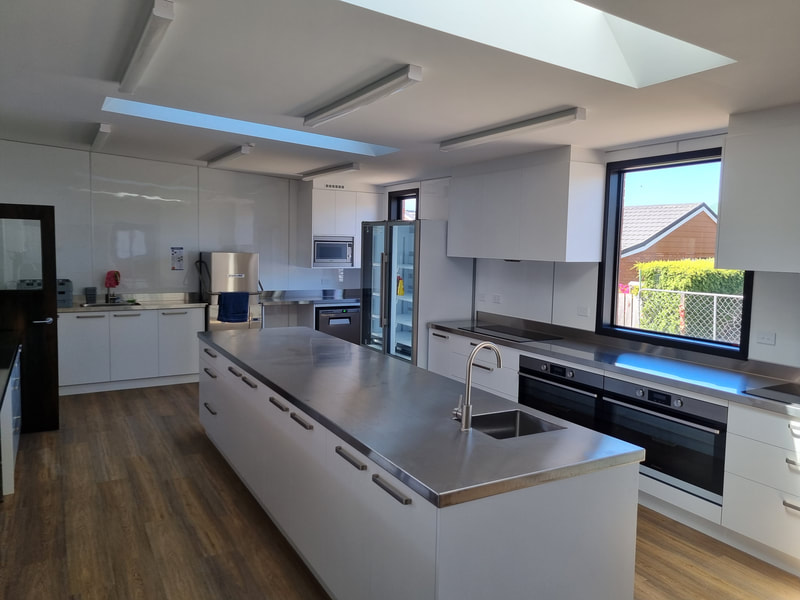 Modern commercial kitchen with stainless steel island bench, ovens and glass-fronted fridge