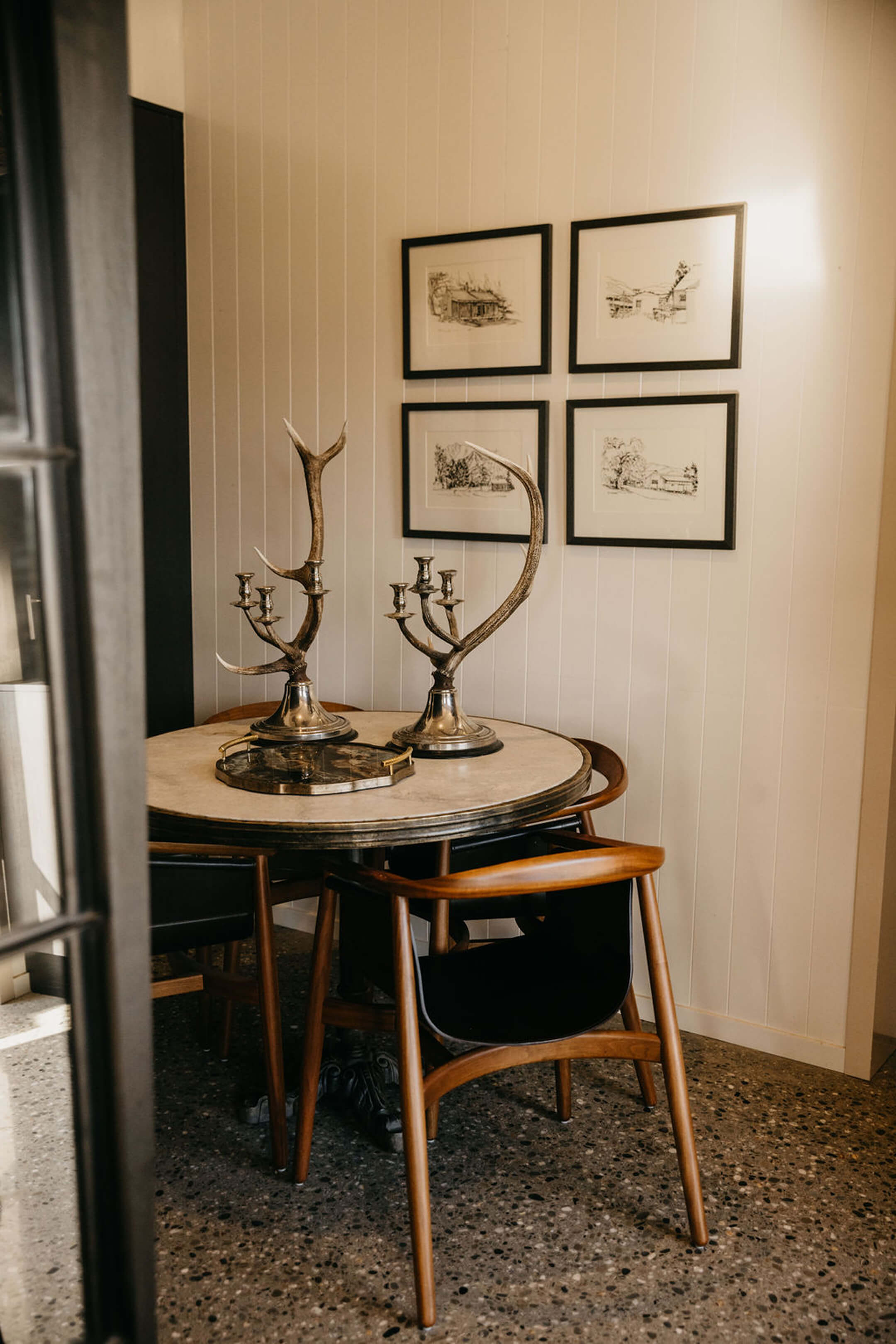 Dining corner with a round marble-top table, mid-century chairs and framed sketches on white timber walls