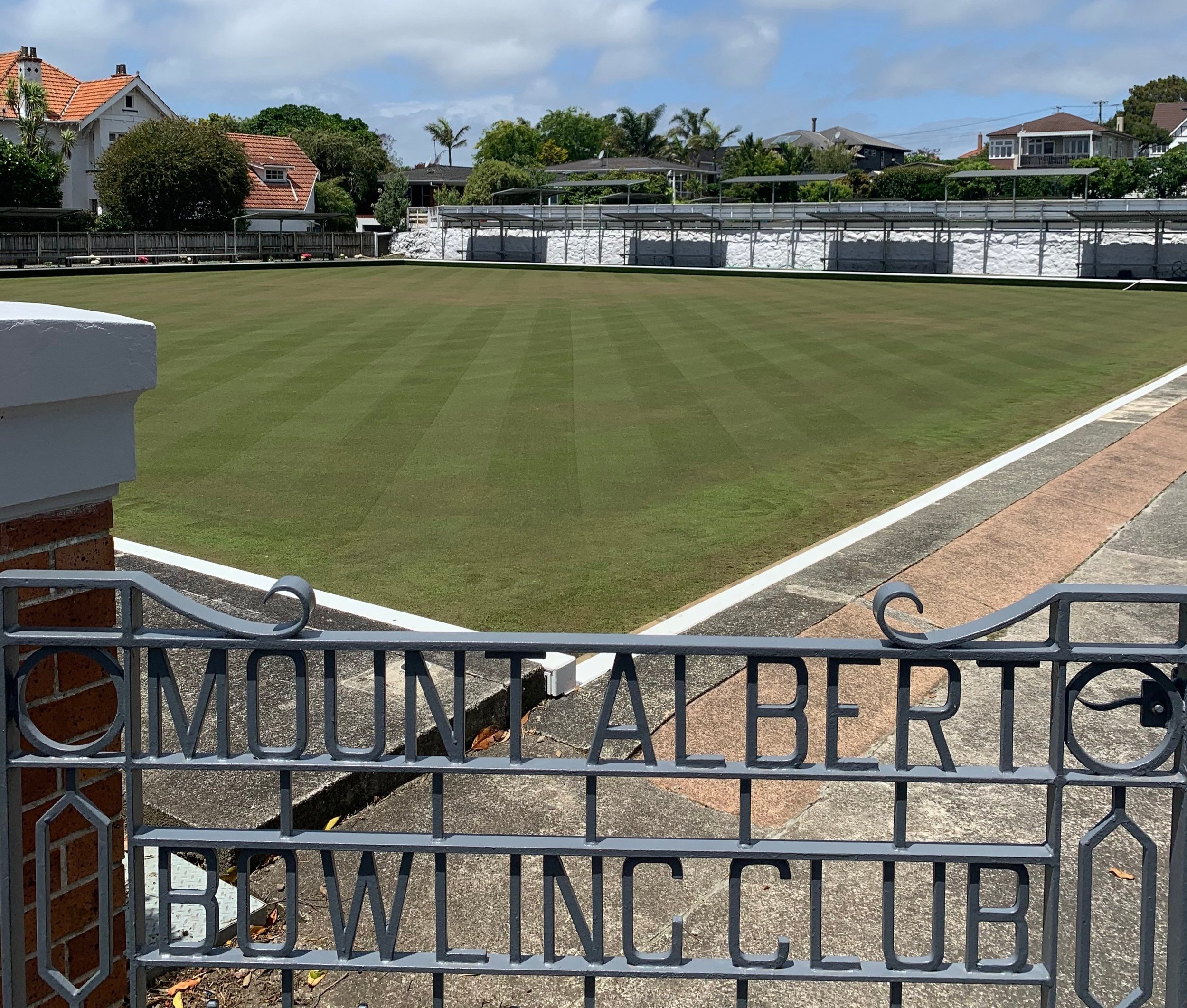 Bowling green and surrounds viewed through ornate metal gates with club name