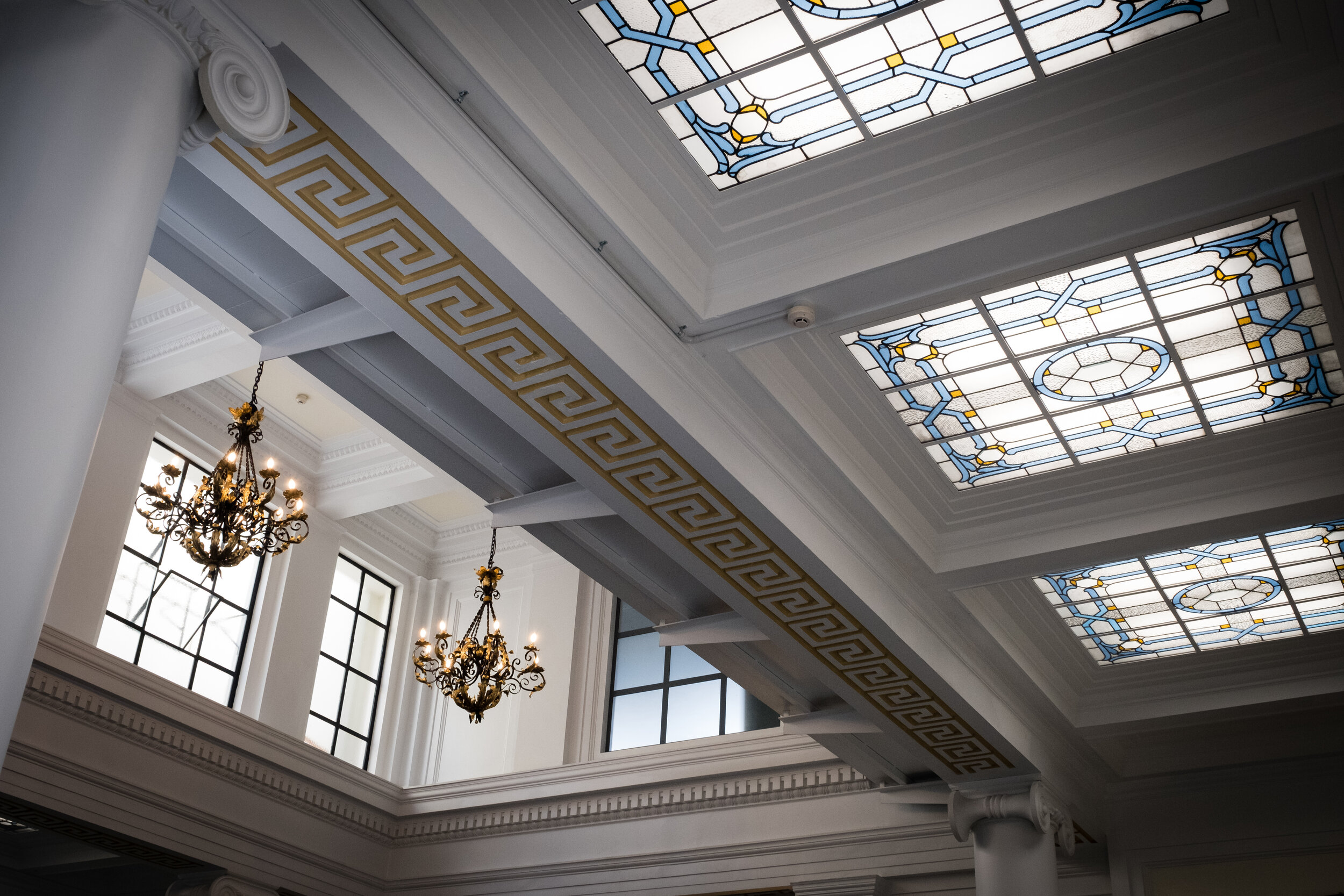Grand hall interior with ornate stained-glass skylights, moulded cornices, and chandeliers