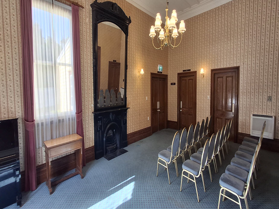 Victorian room with chandelier, wallpaper, fireplace and rows of chairs