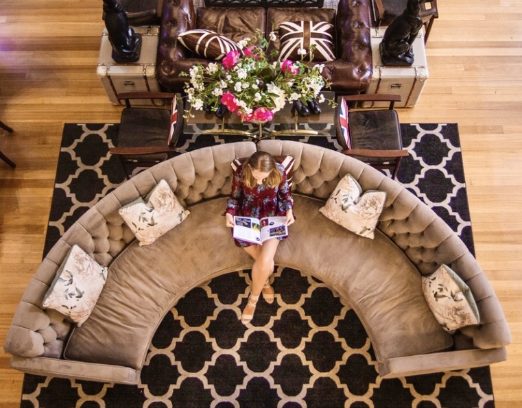 Curved tufted sofa and leather chesterfield on patterned rug, timber floor, overhead view