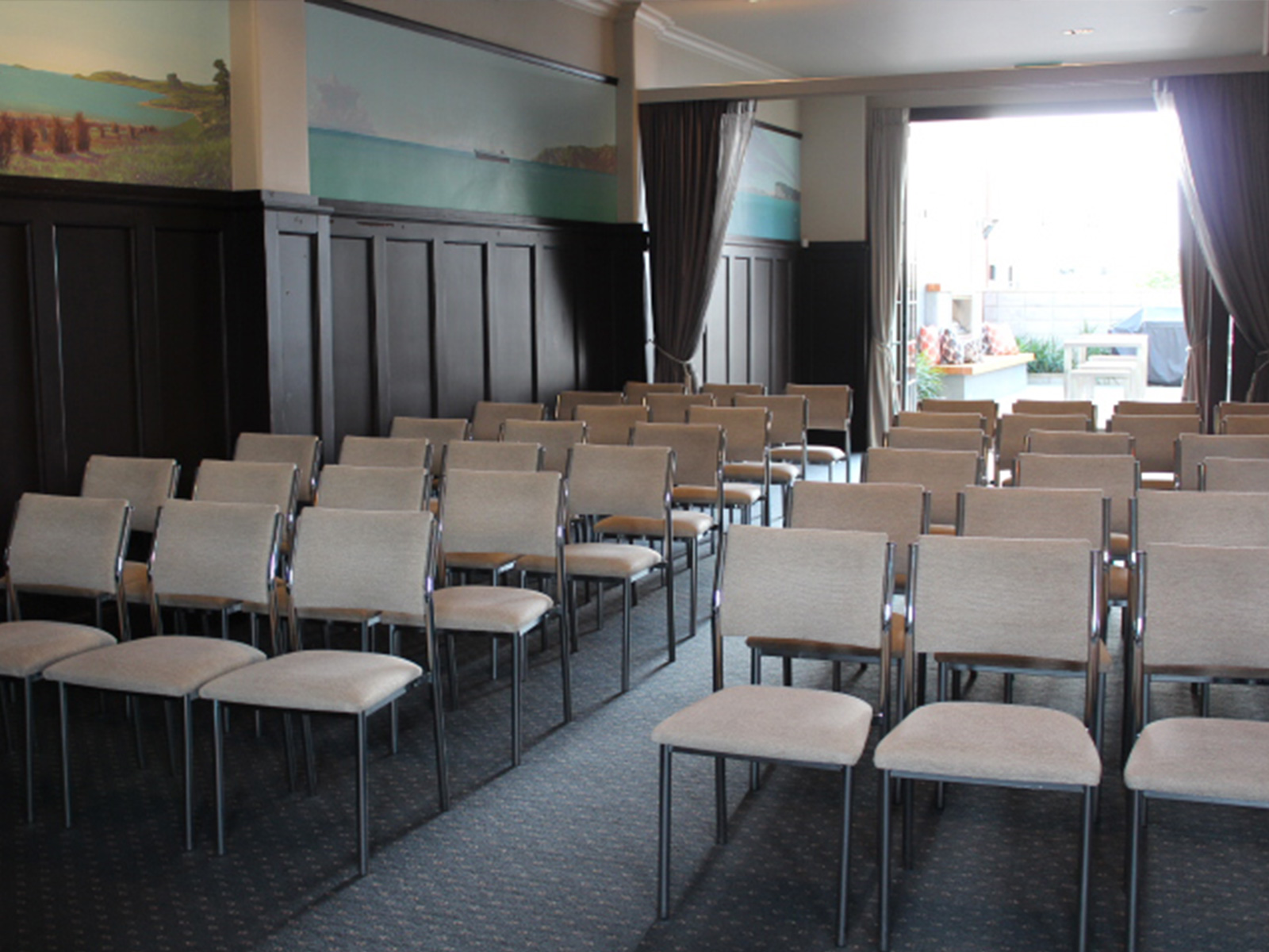 Function room with rows of upholstered chairs, dark timber wall panelling, landscape paintings