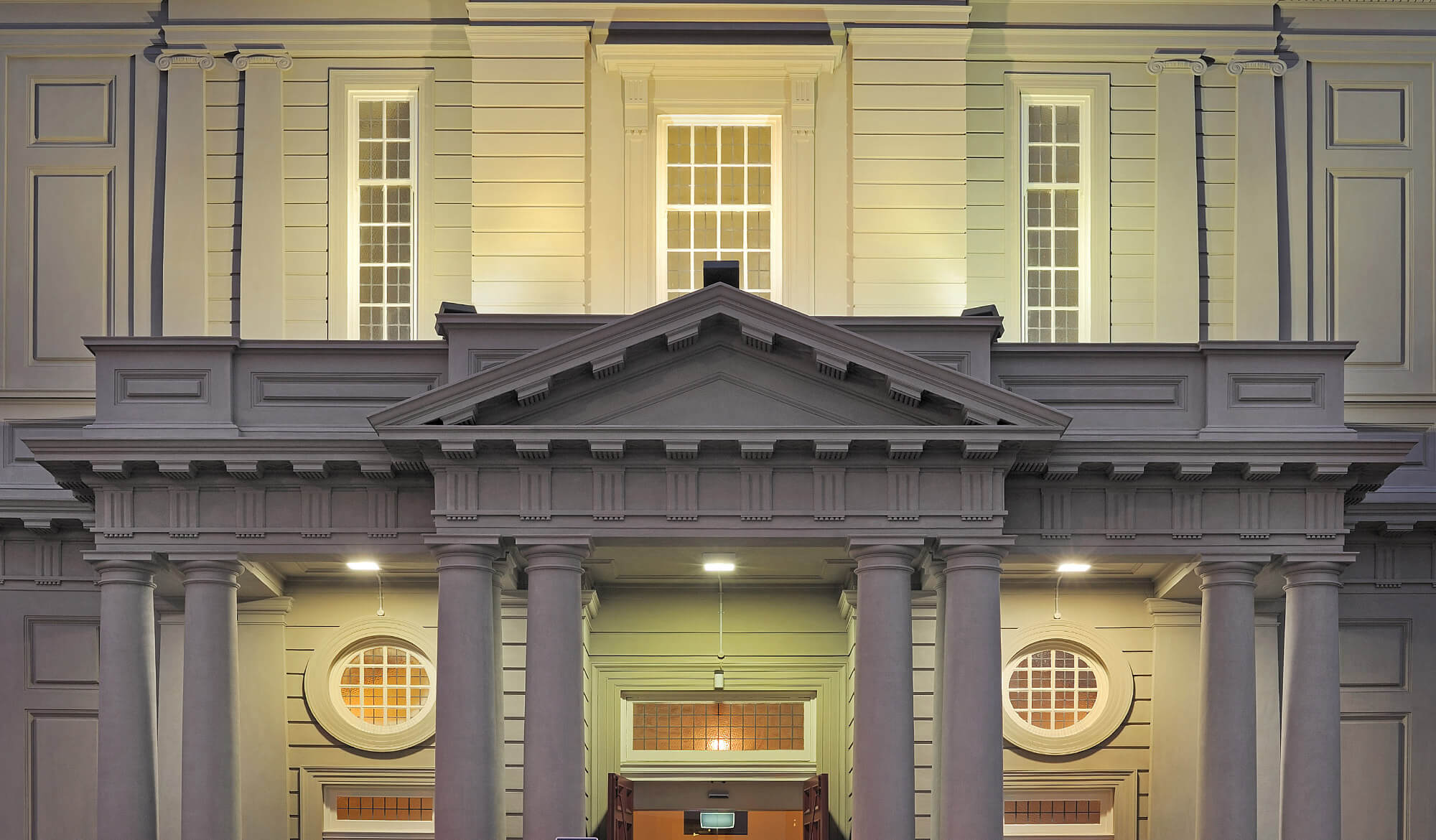 Classical portico facade with columns, triangular pediment, and round windows lit at night