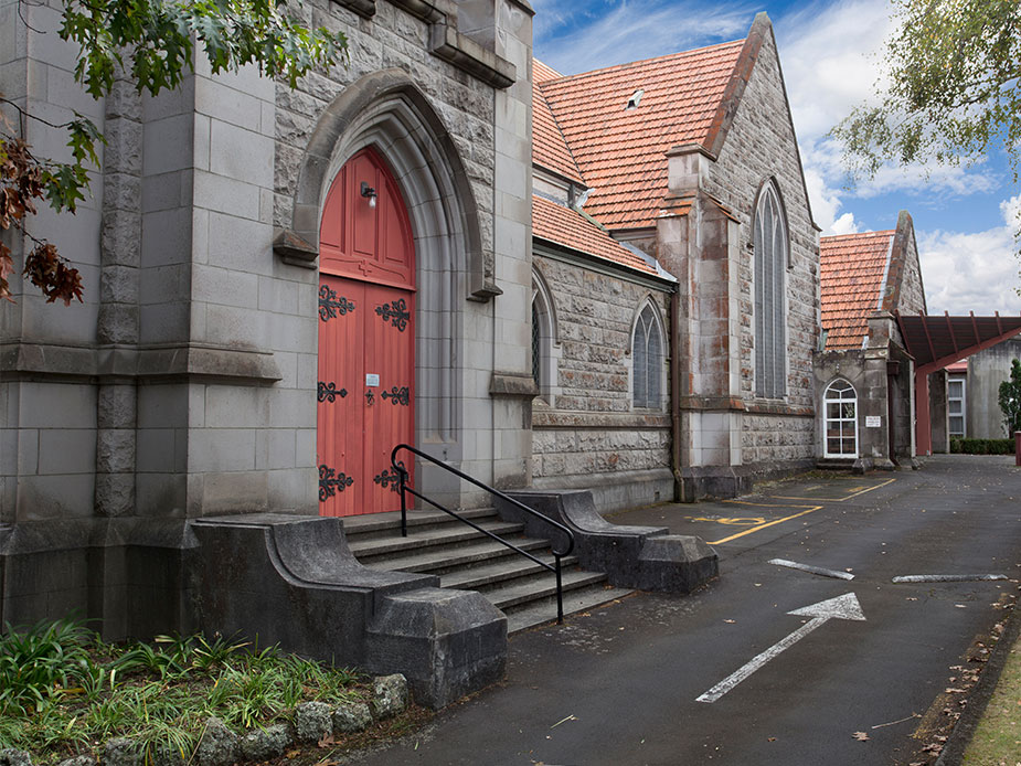 Stone Gothic church exterior with red door, arched windows, and tiled roof