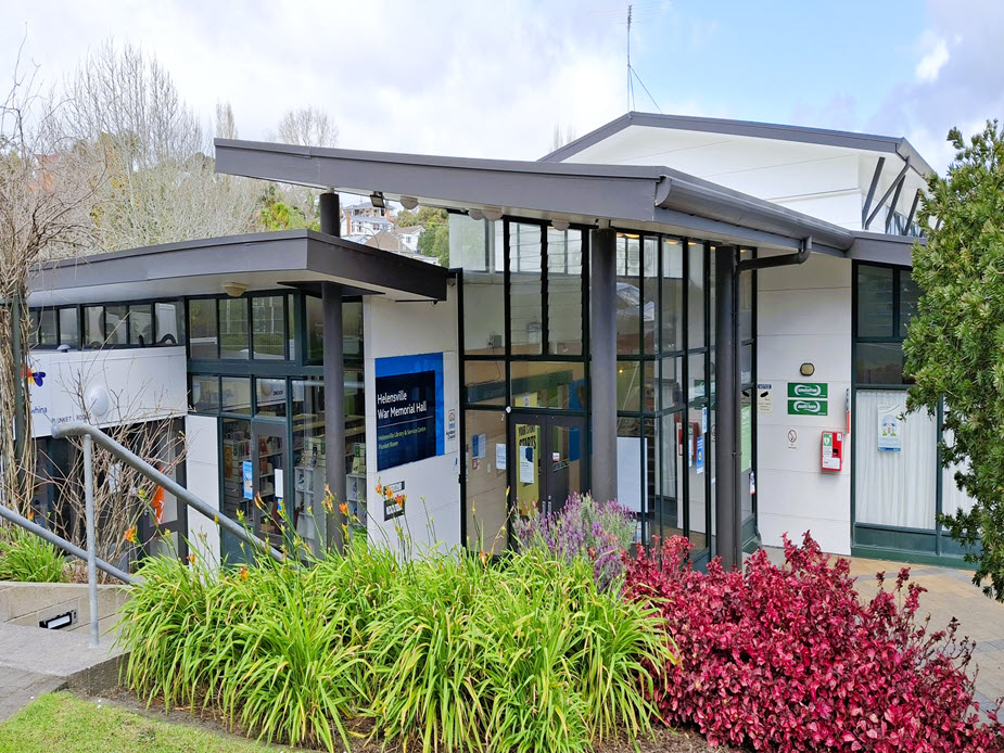 Contemporary glass-fronted community hall building with garden planting, Helensville War Memorial Hall signage visible