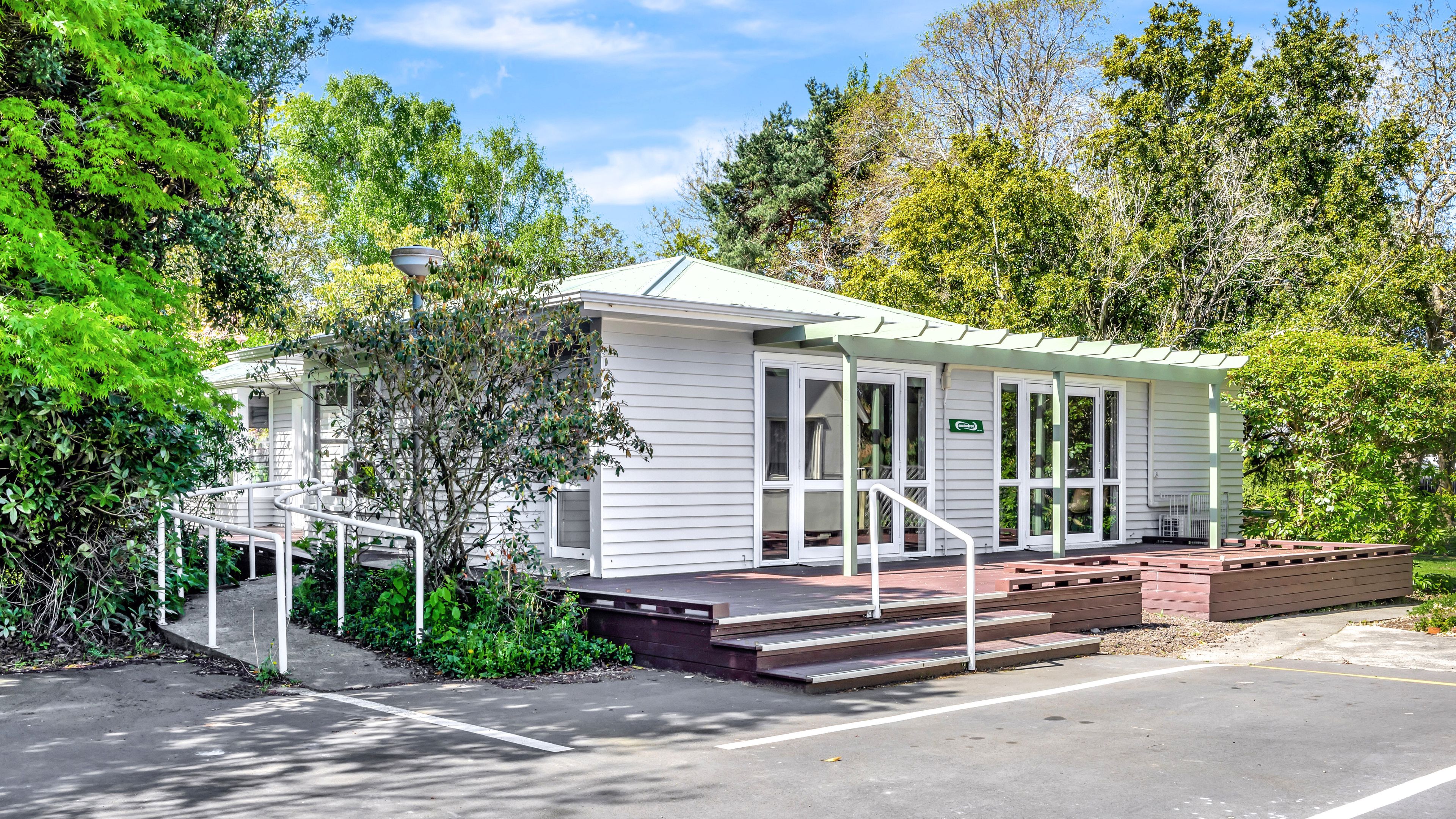 Single-storey weatherboard building with timber deck and ramp entrance surrounded by trees