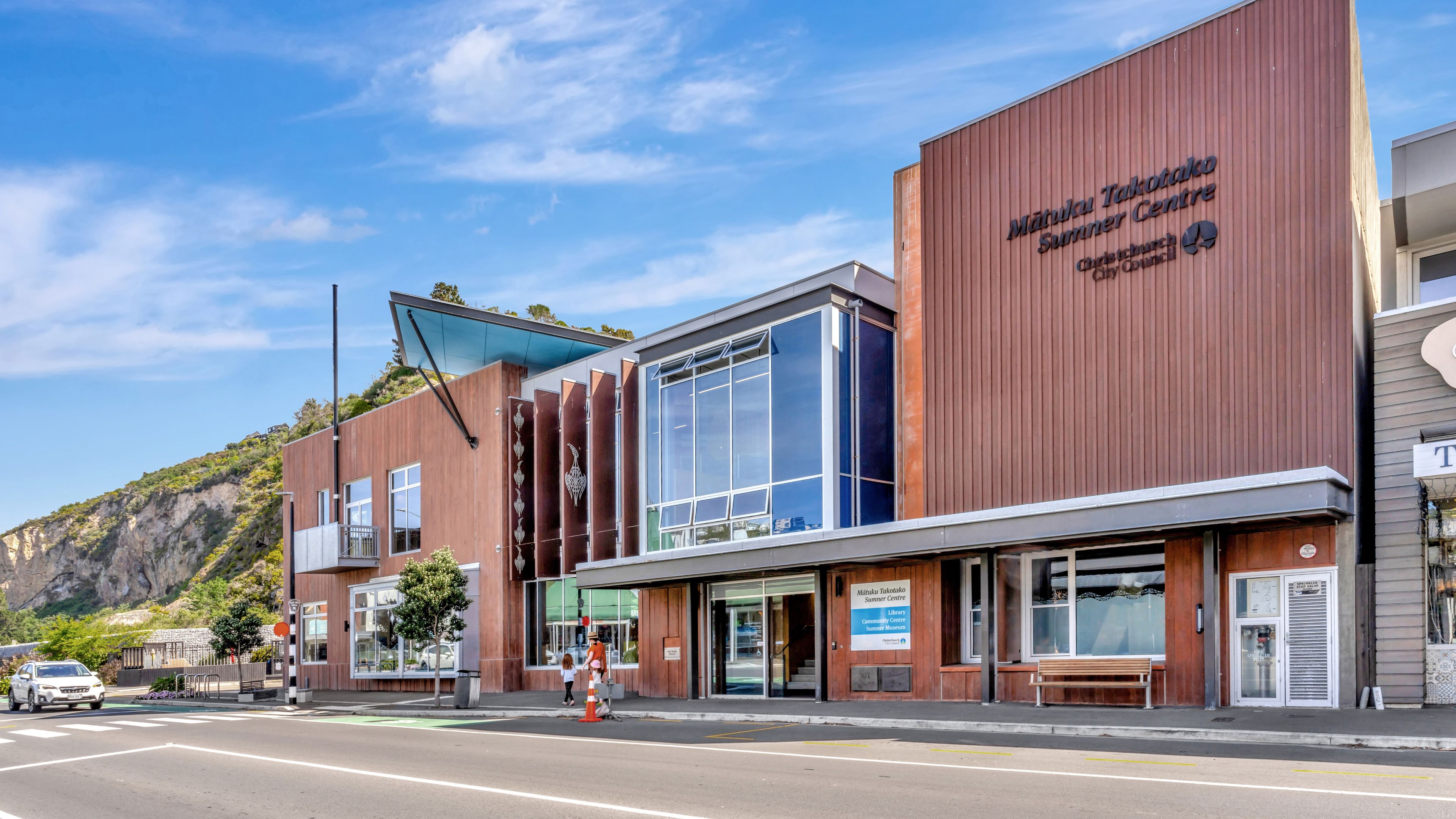 Modern timber-clad community centre building on a town street with hill backdrop