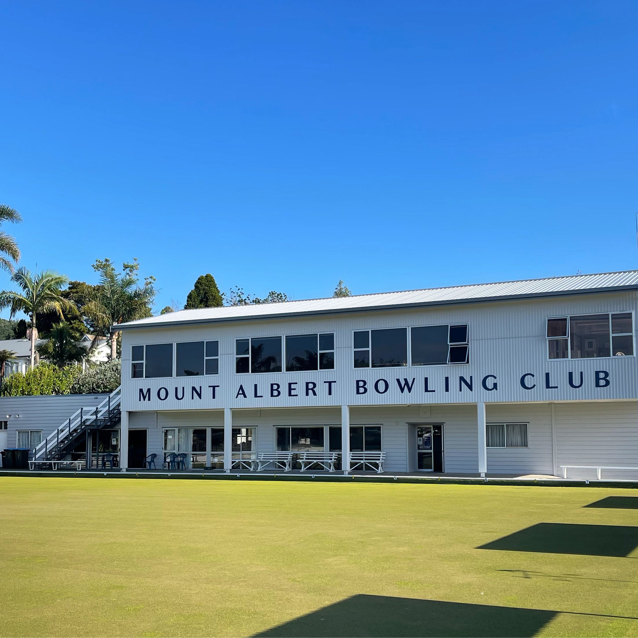 Two-storey white club building beside a flat bowling green