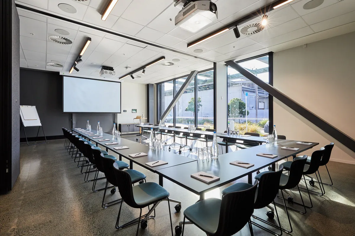 Conference room with U-shaped table arrangement, projector screen, and exposed diagonal steelwork