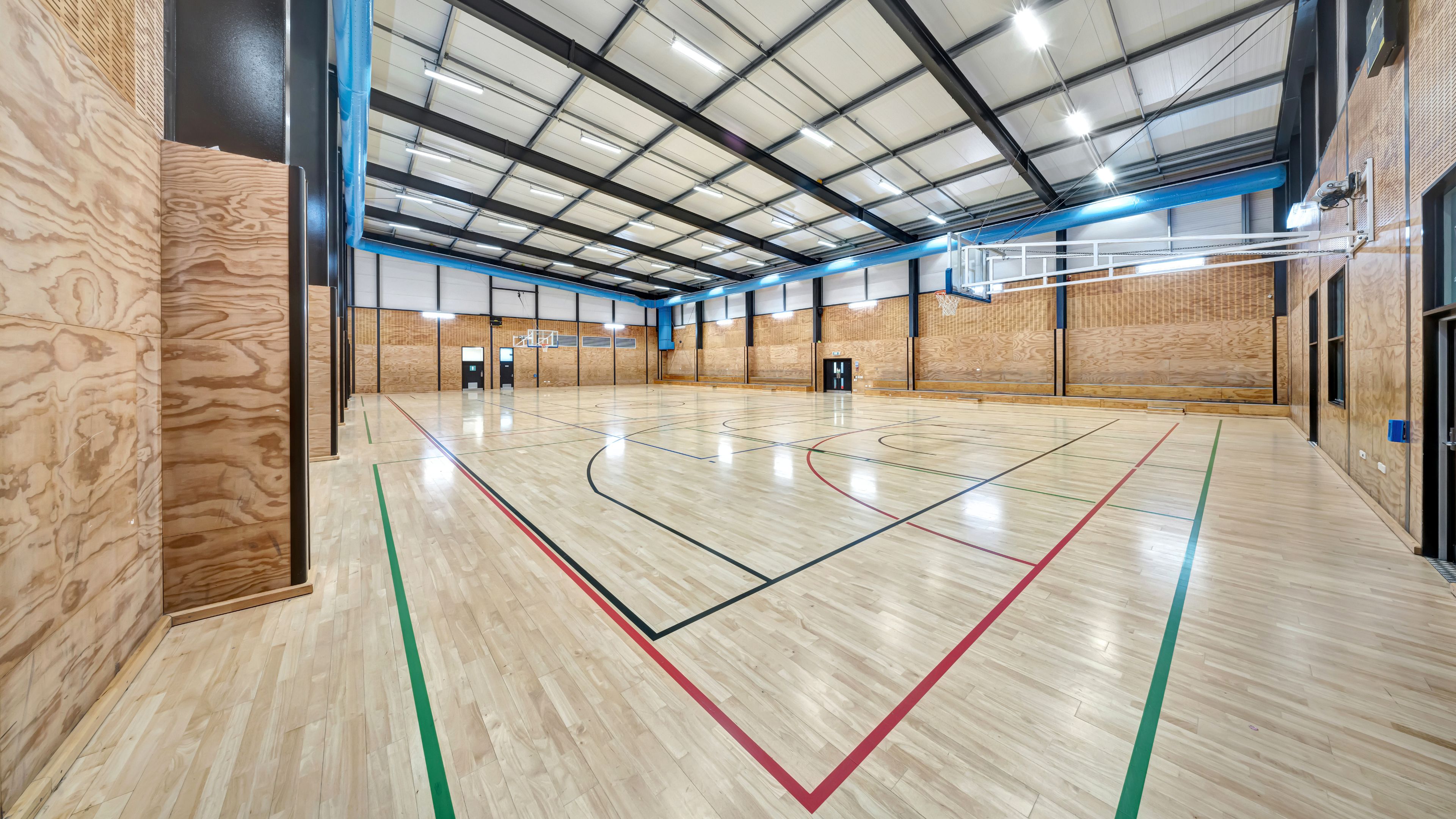 Large indoor sports court with timber floor and blue steel roof structure