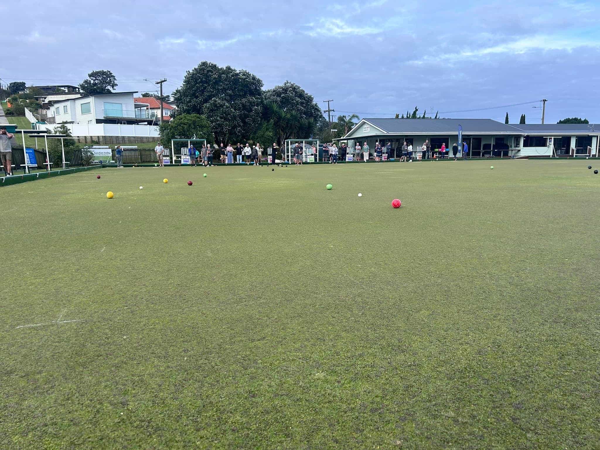 Bowling green with coloured bowls and clubhouse building in background