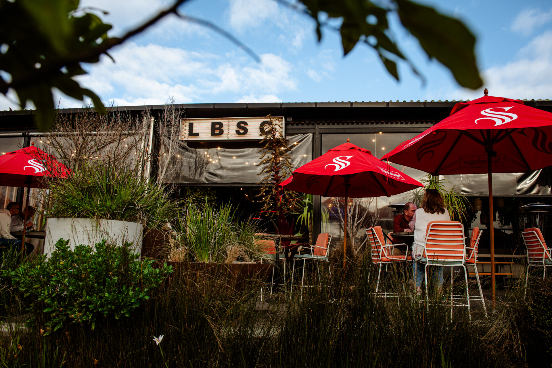 Surf club exterior with outdoor seating, red umbrellas and signage