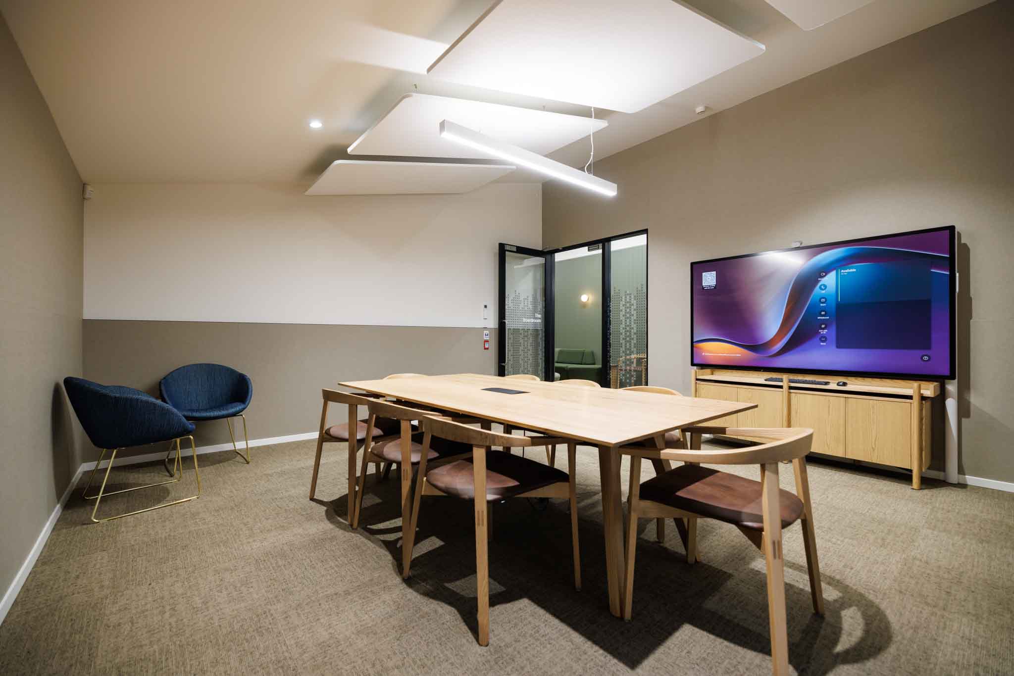 Small meeting room with timber table, chairs, and large wall-mounted screen