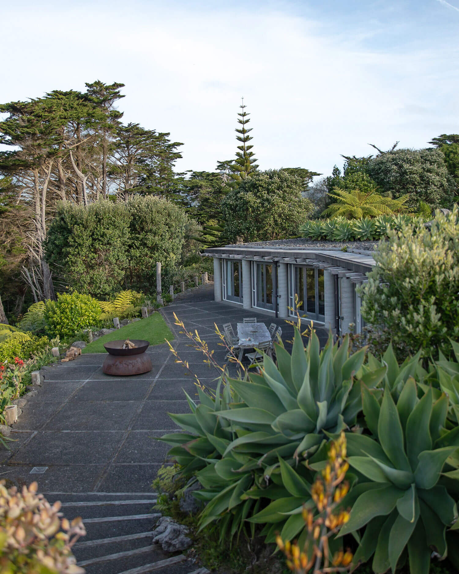 Low curved building with pergola and outdoor dining area set in coastal garden
