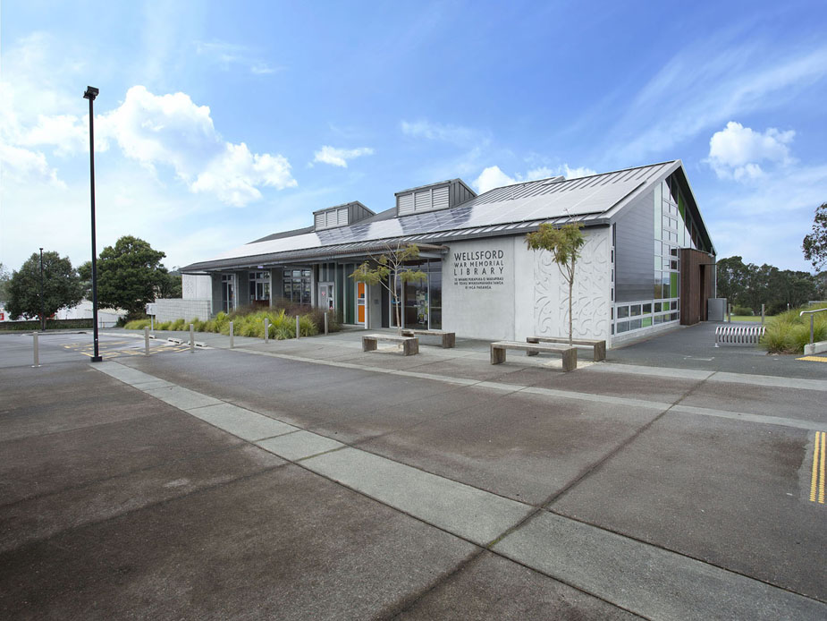 Modern library building with metal roof and decorative panel, car park in foreground