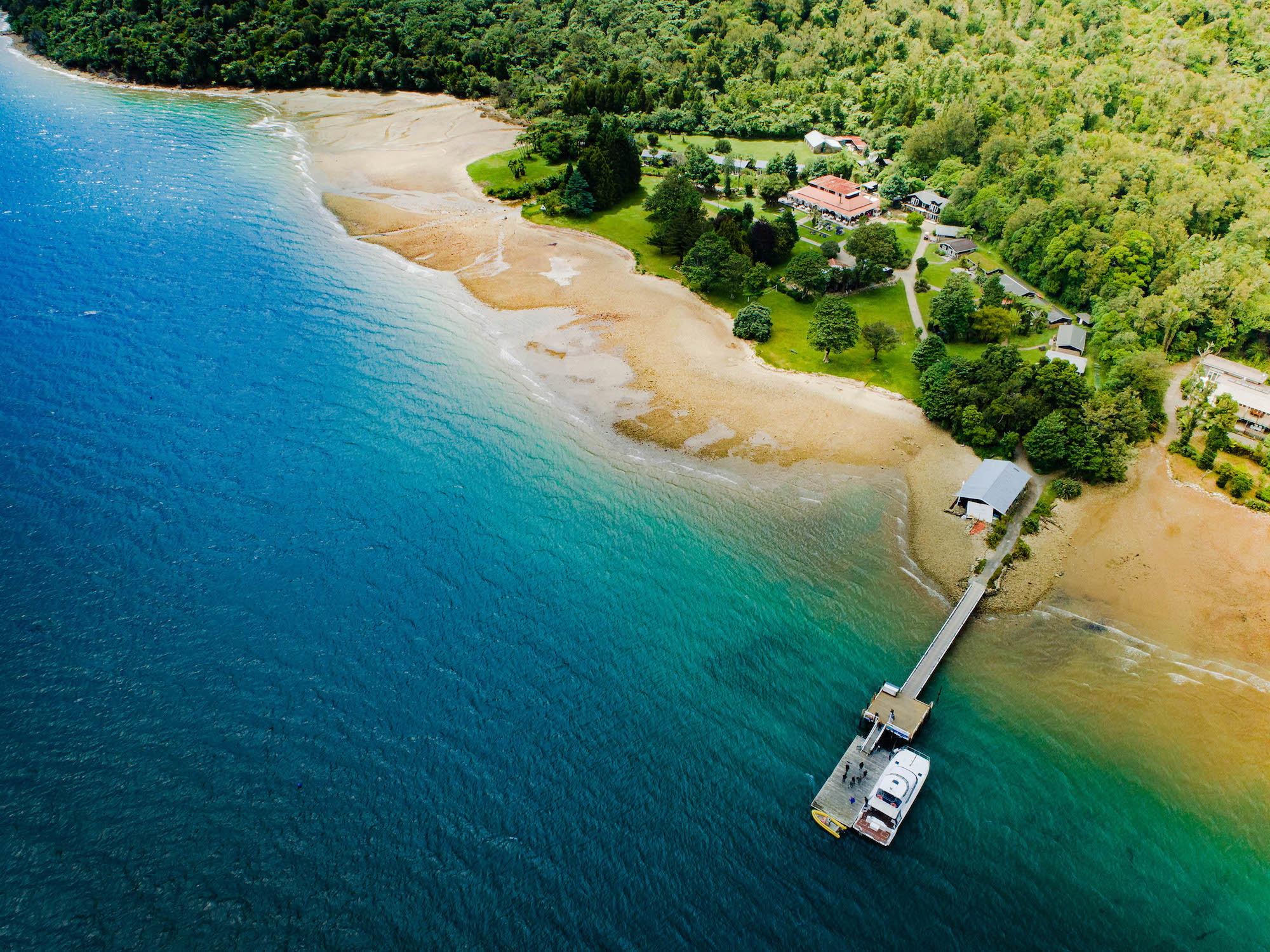 Aerial view of lodge buildings and jetty on sheltered bay with bush