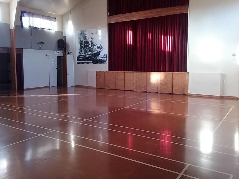 Plain hall interior with polished floor, raised platform behind red drapes at one end