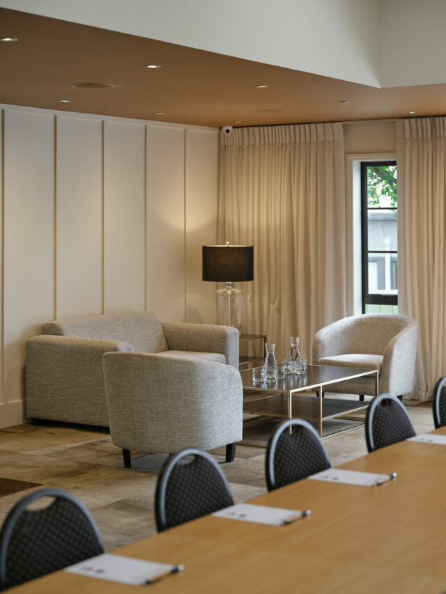 Neutral-toned lounge with two sofas, armchair, floor lamp, and floor-length curtains
