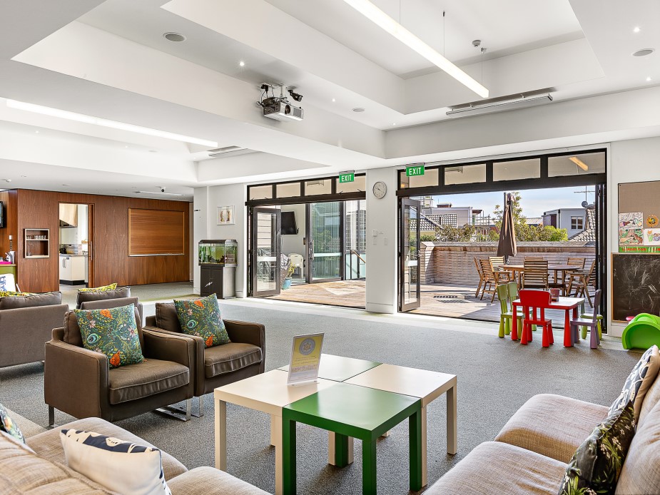 Carpeted lounge with leather sofas, folding doors opening to a timber deck and outdoor seating