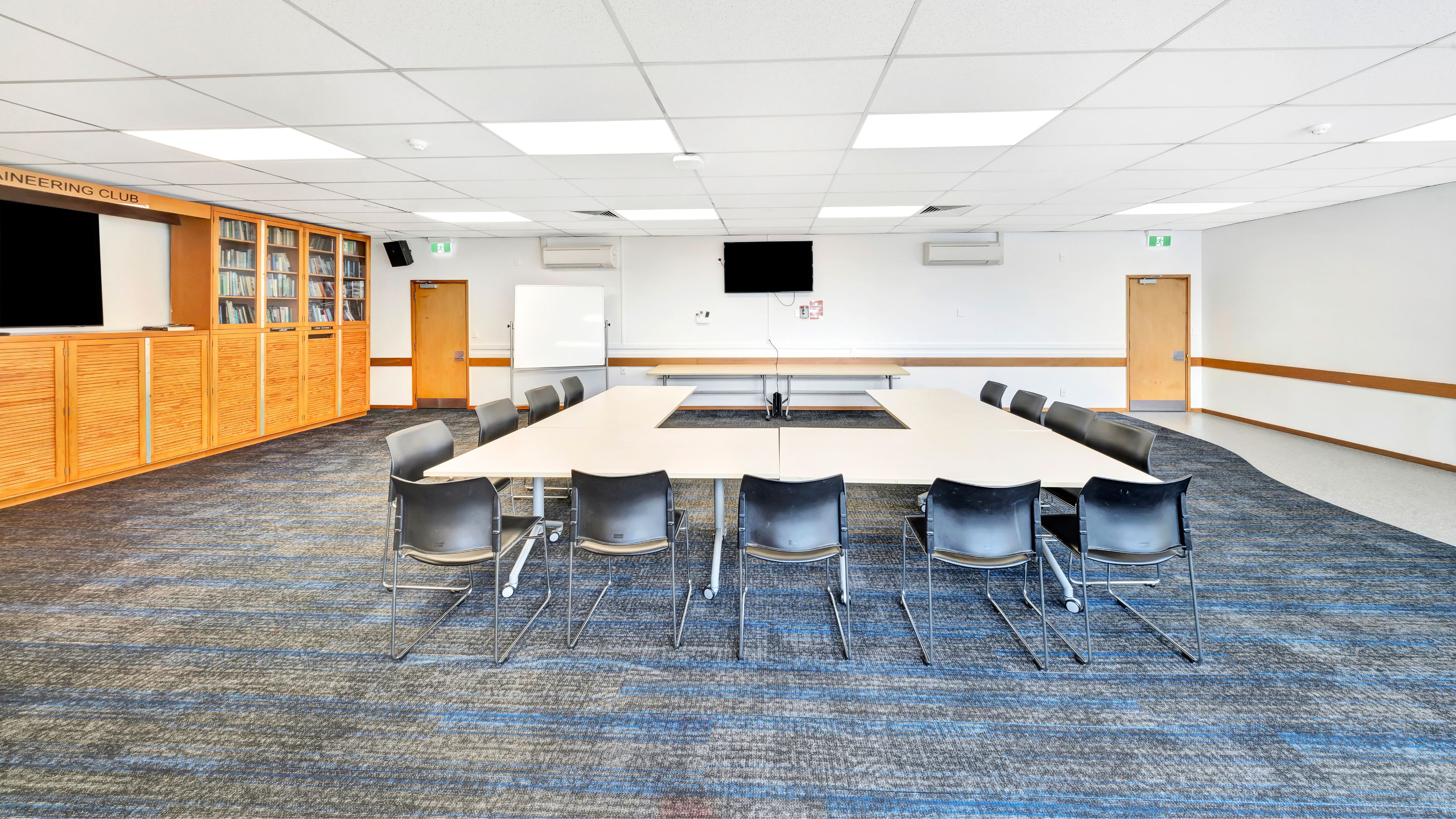 Meeting room with U-shaped table, chairs, bookshelves and wall screens