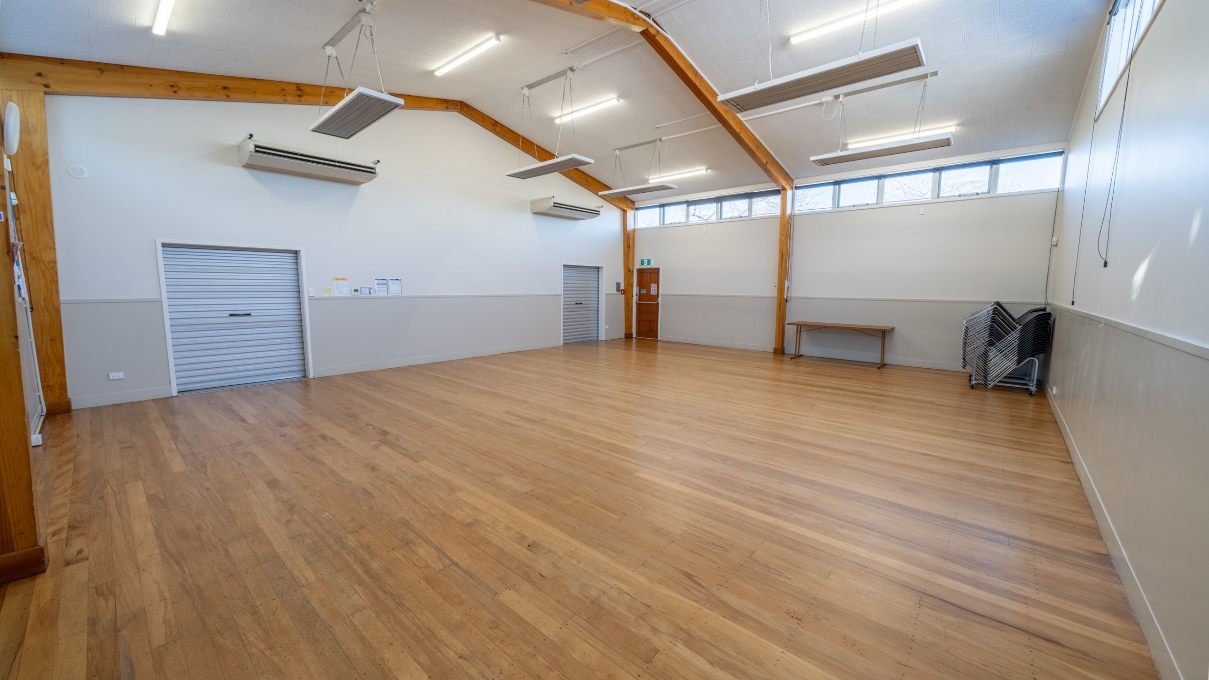 Empty hall with timber floorboards, exposed beam ceiling and roller doors on side wall