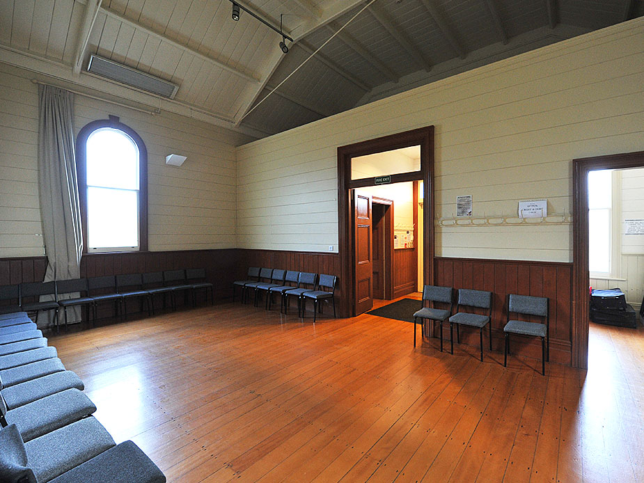 Timber-lined hall interior with arched window, polished floor, and scattered chairs