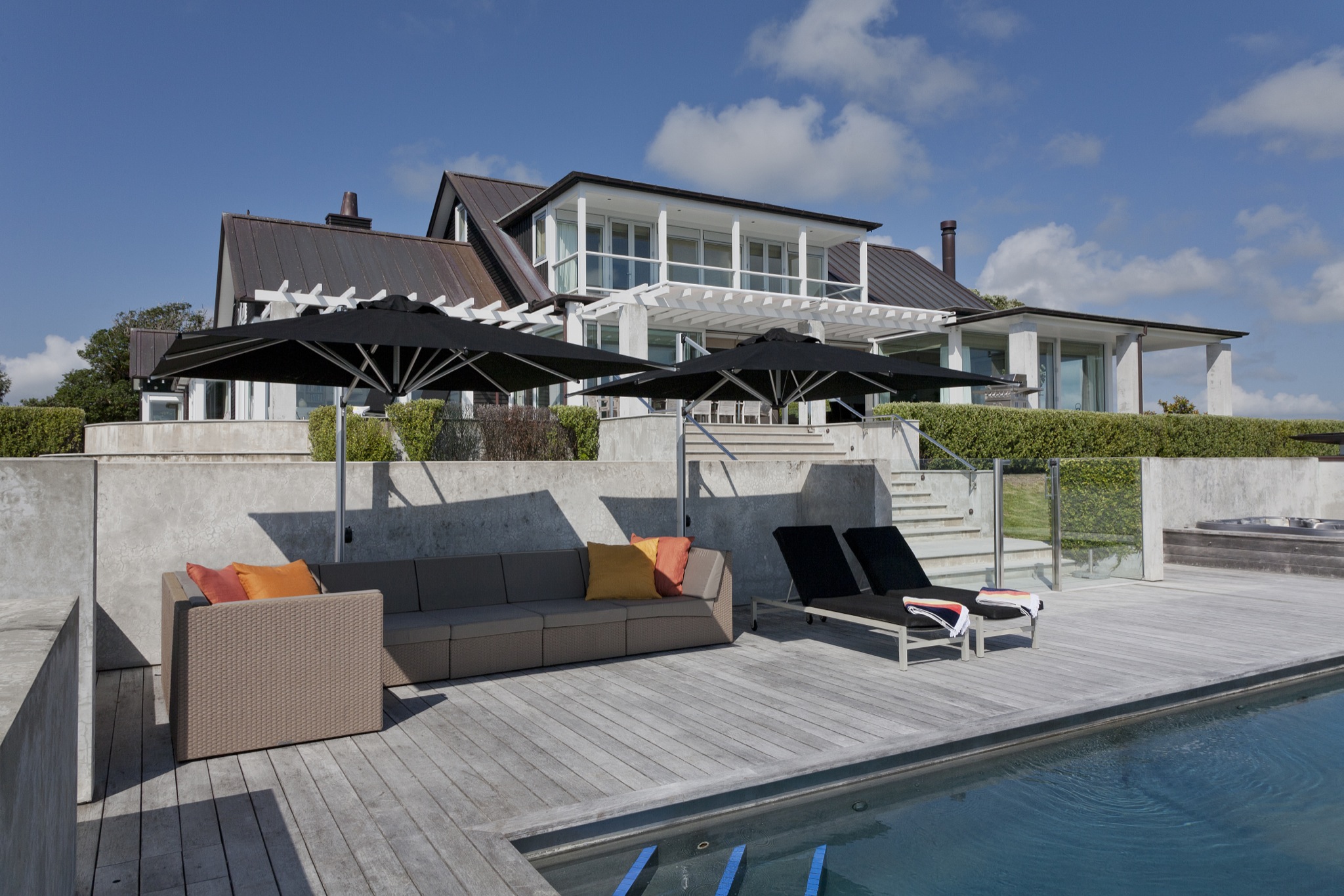 White render house with dark roof, pool terrace, deck furniture, and pergola beyond