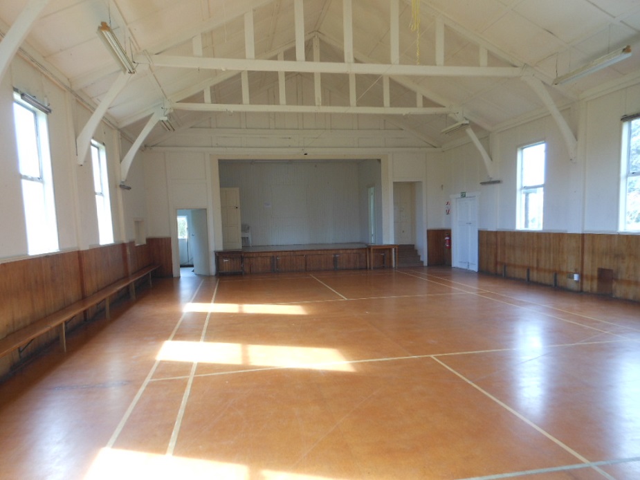 Empty hall interior with timber-panelled walls, raked timber-truss ceiling, raised platform at far end