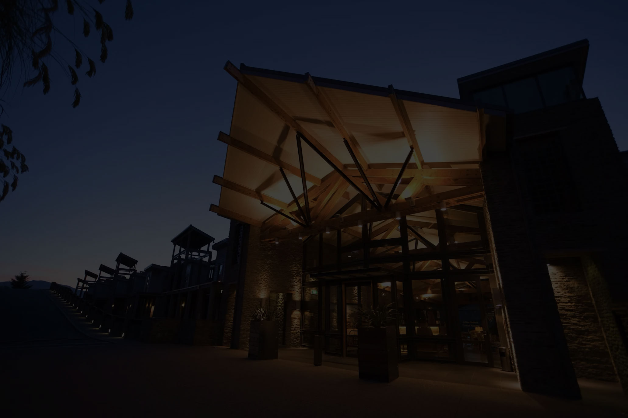 Dark building with large timber canopy over entrance, lit from below, stone cladding at night