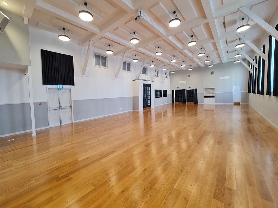 Spacious timber-floored hall with white coffered ceiling, pendant lights, and black-framed windows