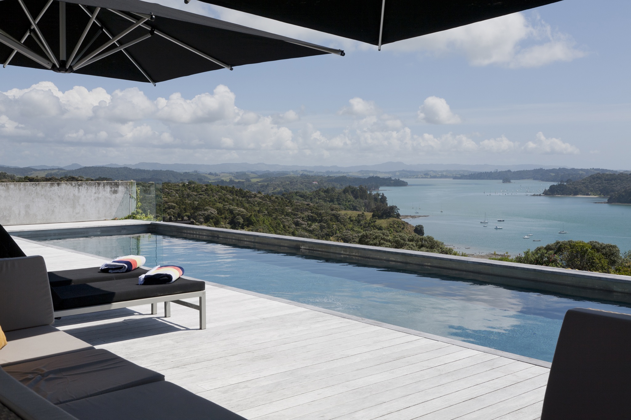 Concrete pool terrace with sun loungers, large shade umbrella, and coastal bay view