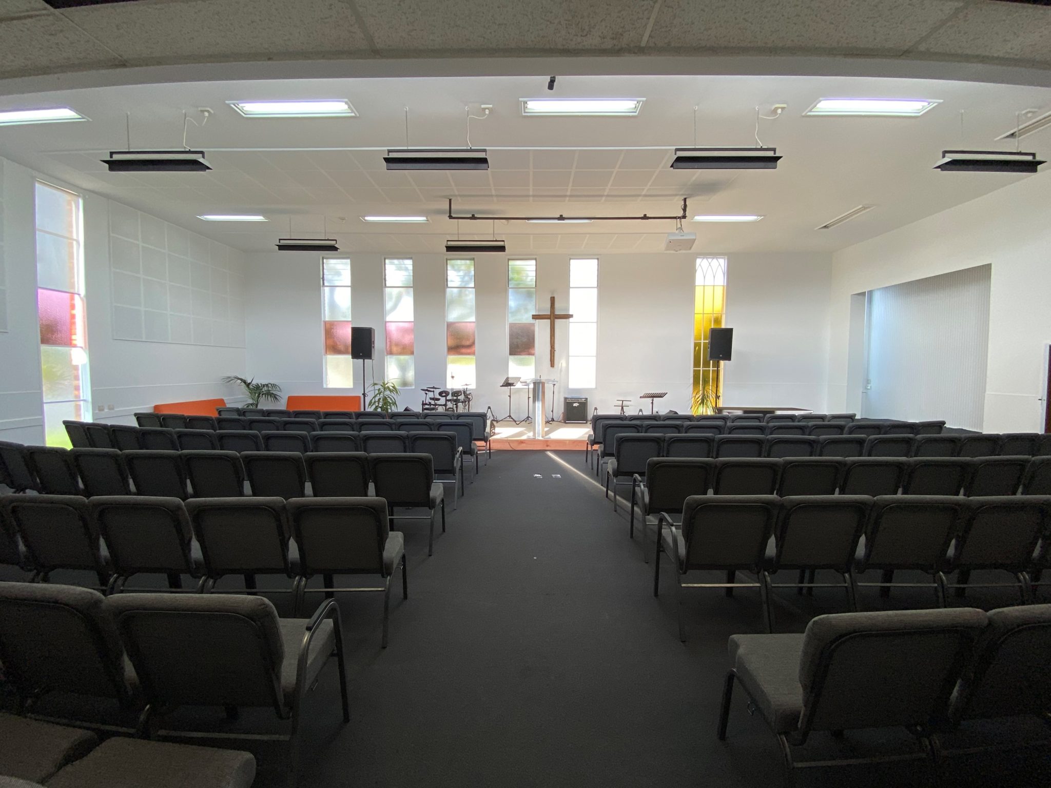 Church sanctuary with rows of chairs, cross at front and coloured window panels