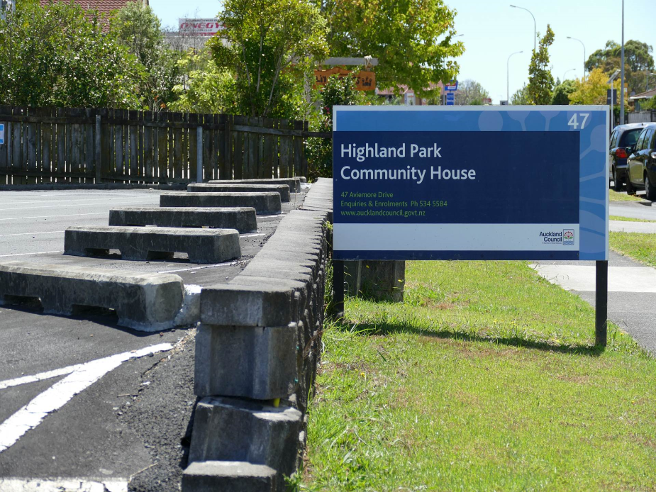 Street-facing sign reading Highland Park Community House with car park and fence visible