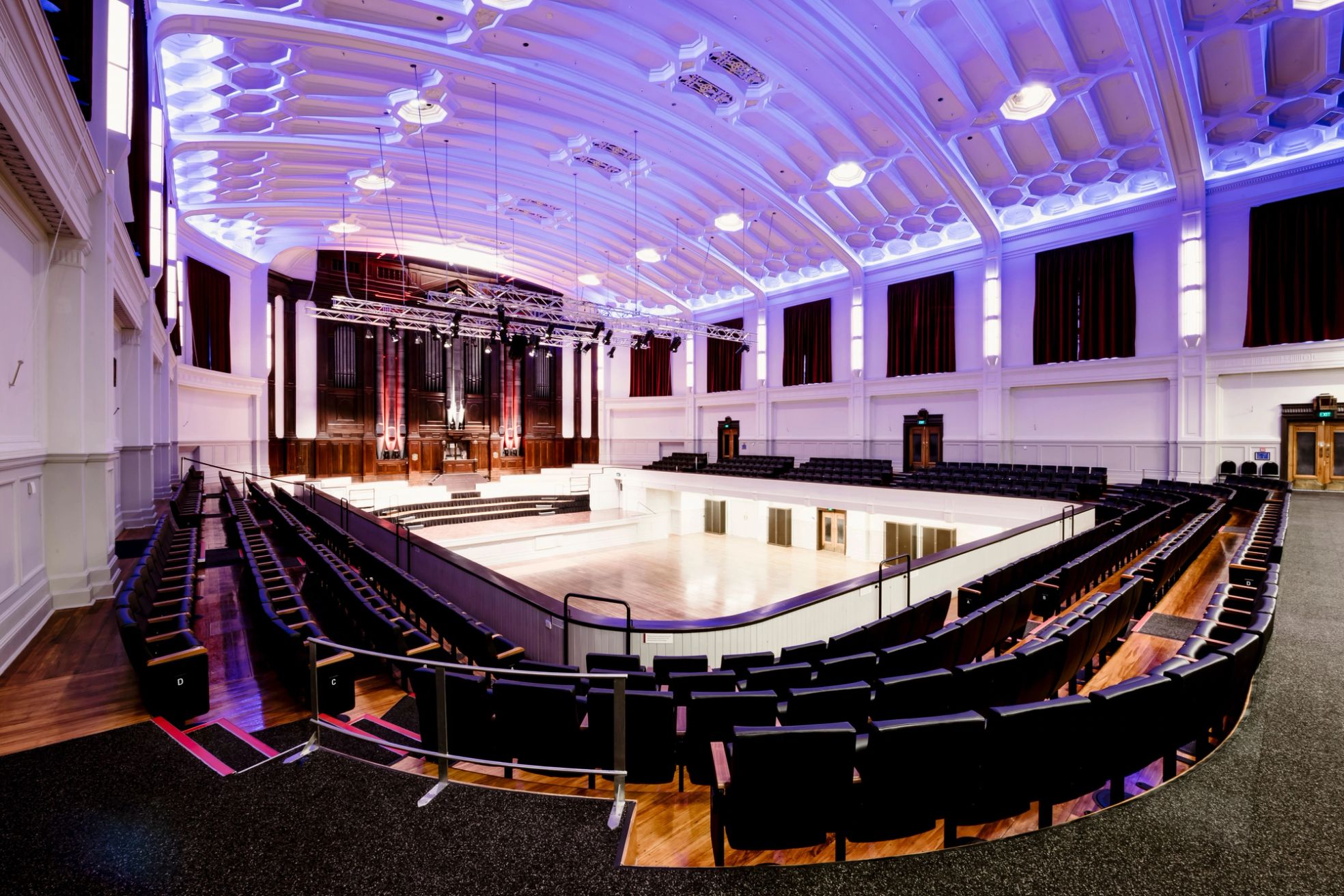 Grand auditorium with tiered seating, ornate white ceiling and pipe organ