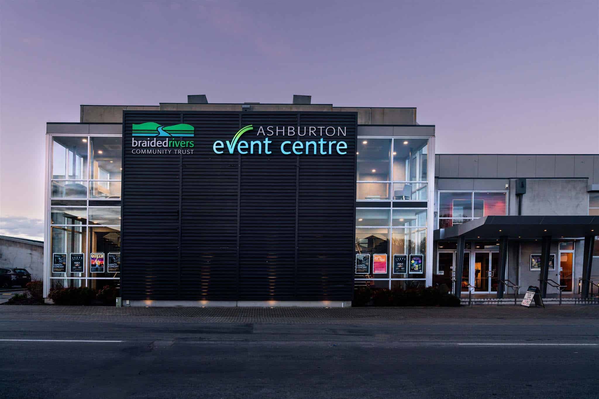 Modern event centre exterior at dusk with illuminated signage on dark cladded facade