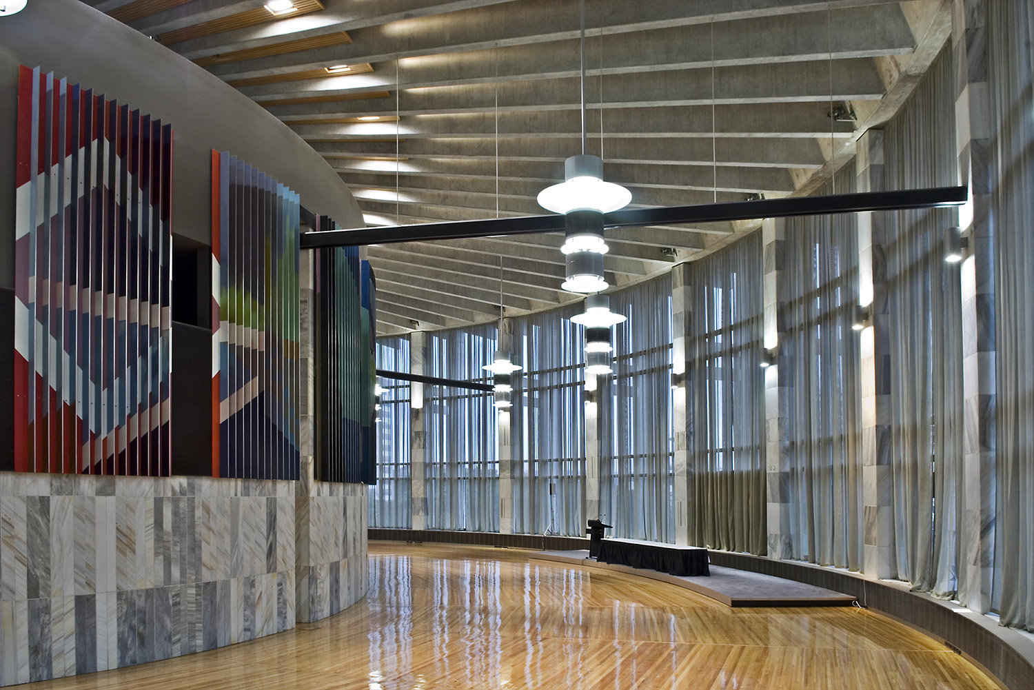 Curved hall with timber floor, marble-clad wall, hanging pendant lights and sheer curtained windows