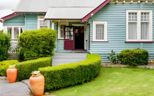 Blue weatherboard villa with hedged front garden and covered entrance