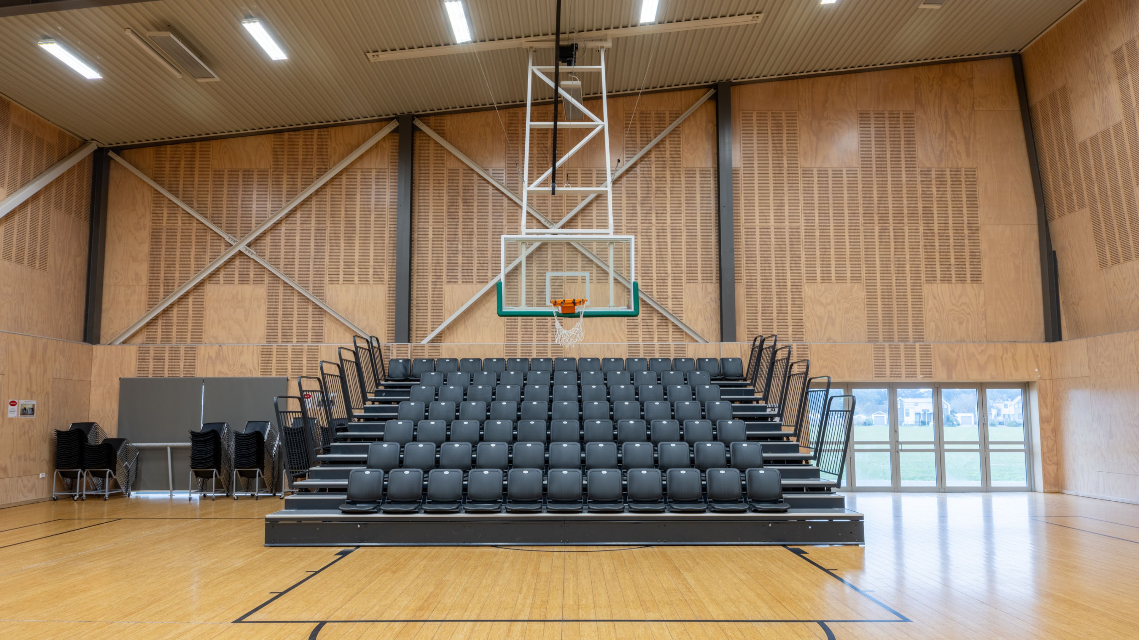 Sports hall with bleacher seating and basketball hoop on timber floor