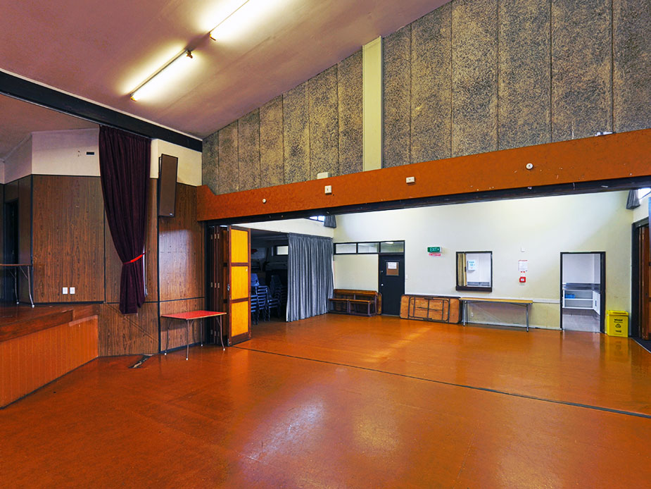 Hall main room with orange vinyl floor, raised platform and dark timber panelling