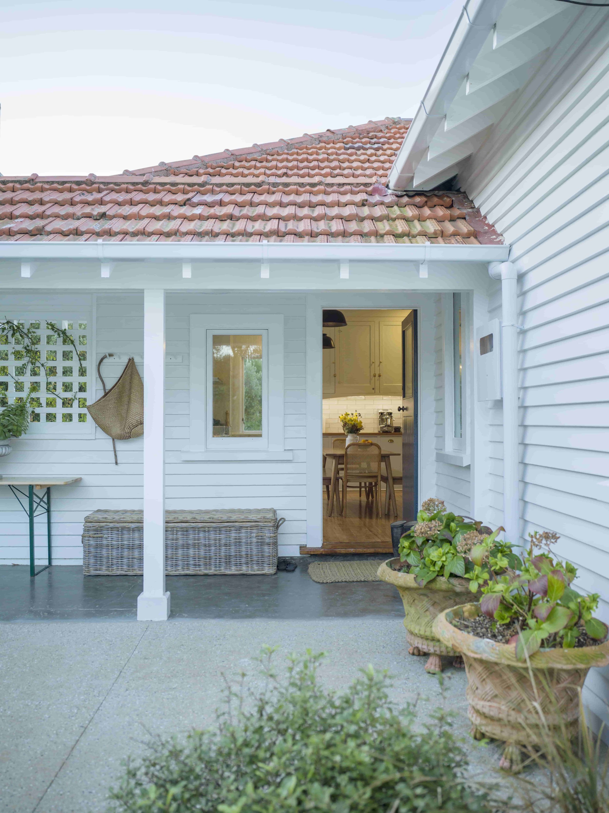 White weatherboard house with covered entry porch, terracotta tile roof and potted plants