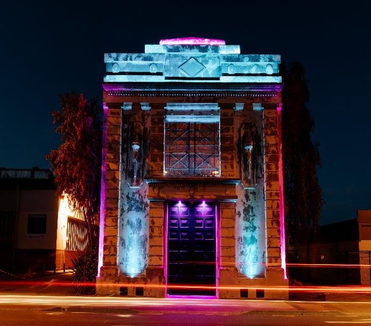 Historic stone building with classical columns lit with coloured lighting at night