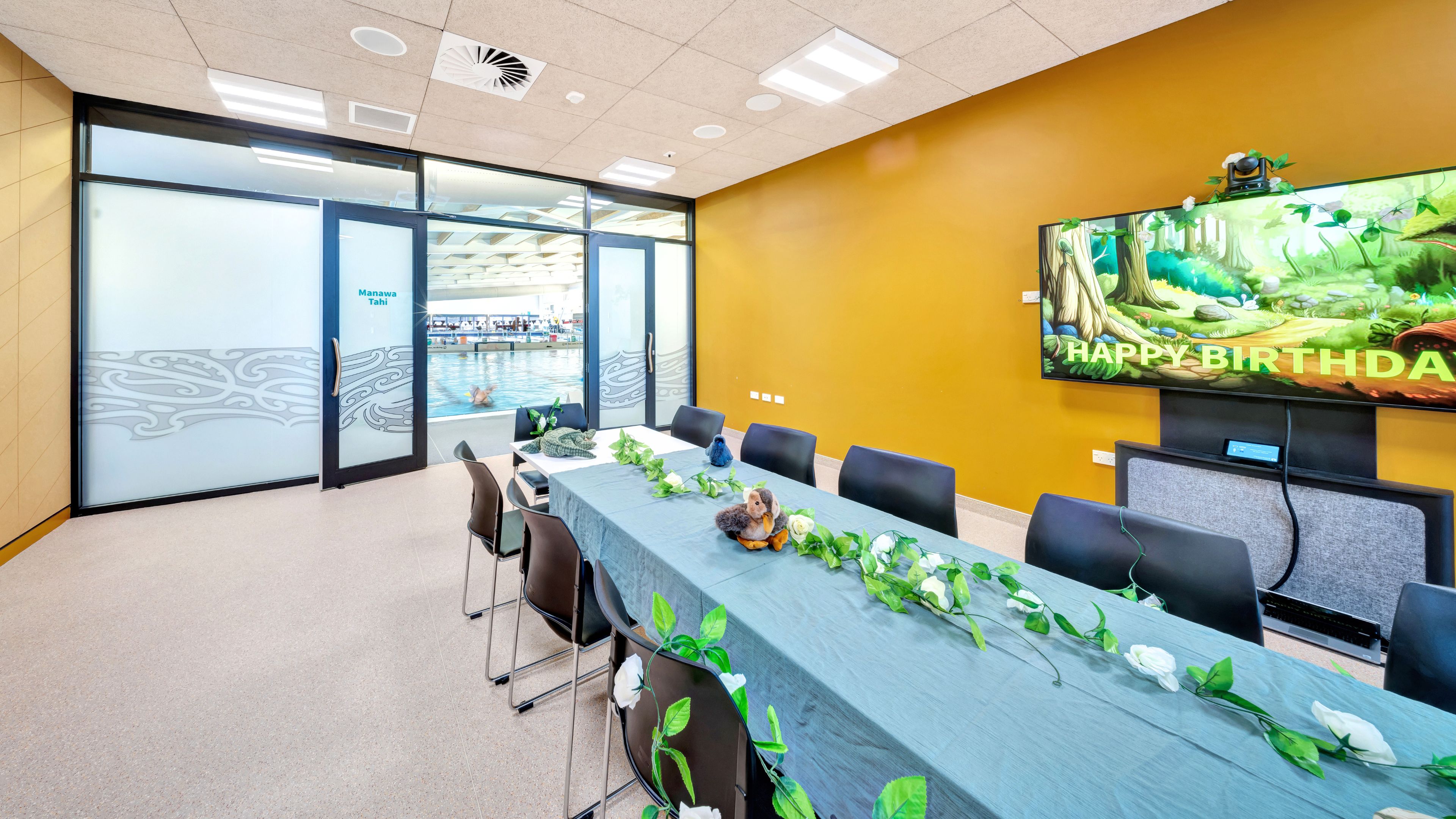 Meeting room with long table, chairs and large display screen on yellow wall