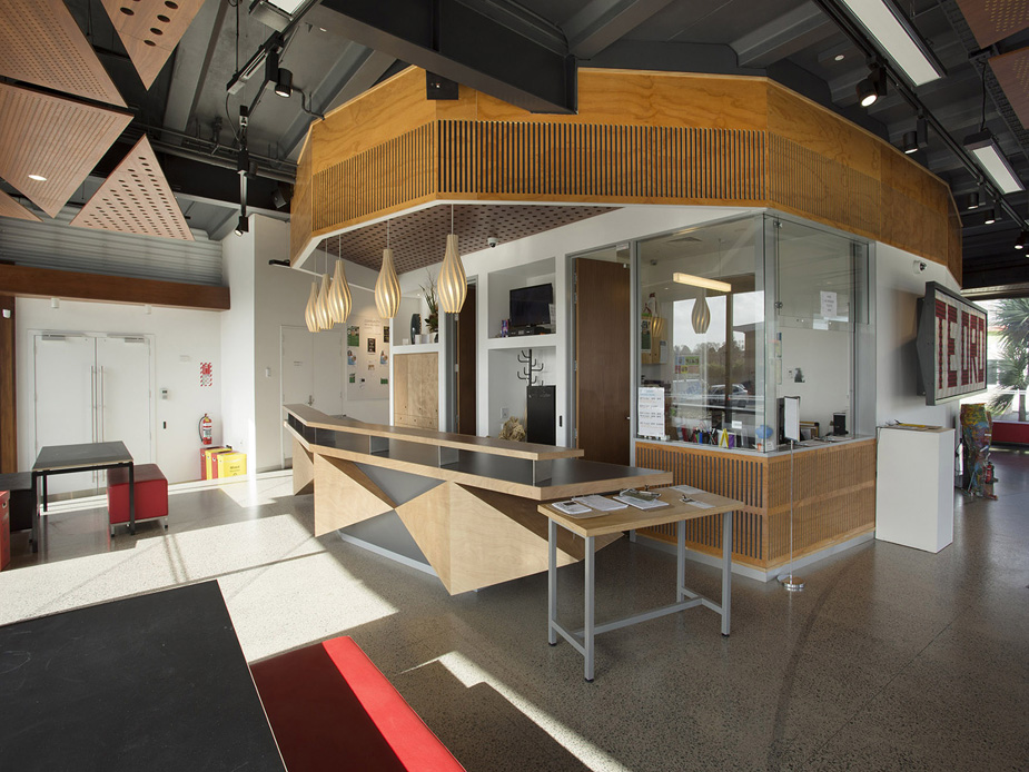 Curved plywood interior wall with cork floor, geometric ceiling panelling, and full-height glazing